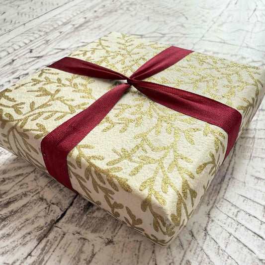 Gift box with gold leaf pattern and red ribbon on a wooden surface