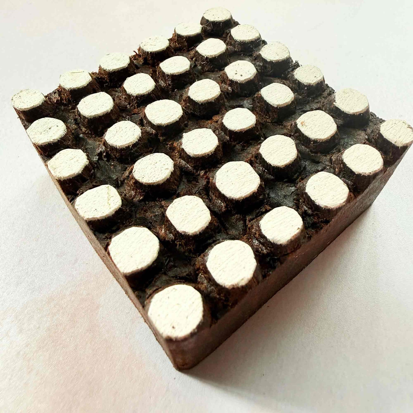 Hand-carved Spotty Indian wood block stamp — square grid of rounded dots face-on view on soft pale background, traditional dotted printing block close-up