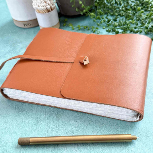 Brown leather notebook with a pen on a light blue surface with plants in the background
