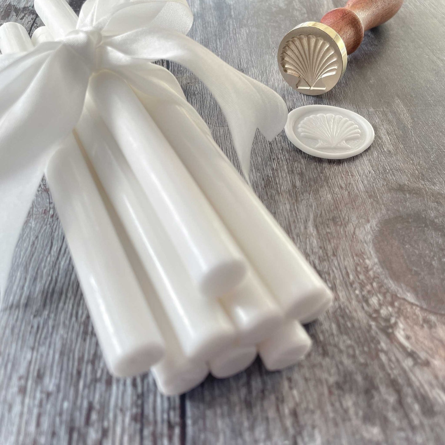 White eco friendly sealing wax sticks. Make wax seals with a wax seal stamp. The seashell wax stamp shown in the image has a brass head and a wooden handle. Perfect for making coastal wax seals. By The Natural Paper Company
