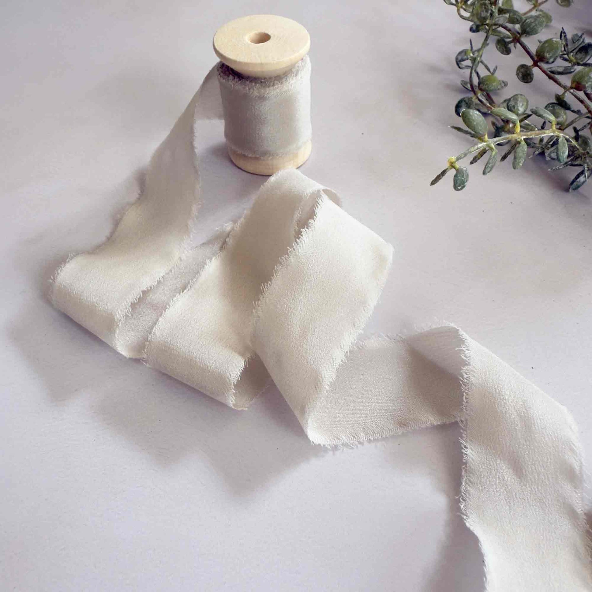 Beige silk ribbon with a raw edge.  Fine silk ribbon on a wooden reel