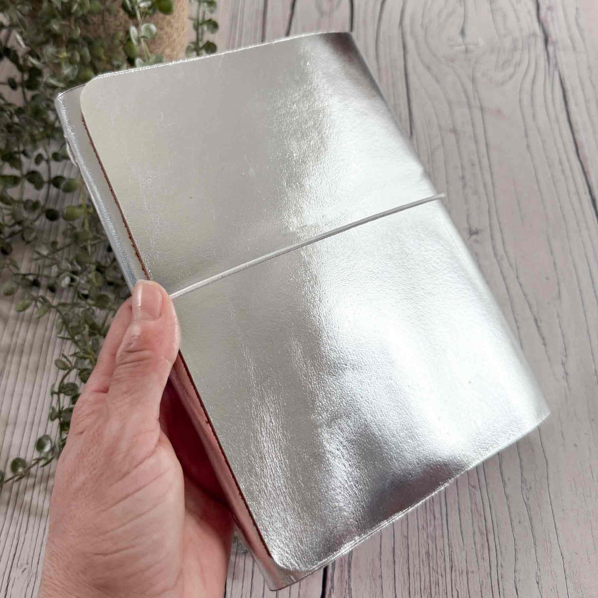 Metallic silver refillable A5 leather journal held by hand showing reflective leather finish