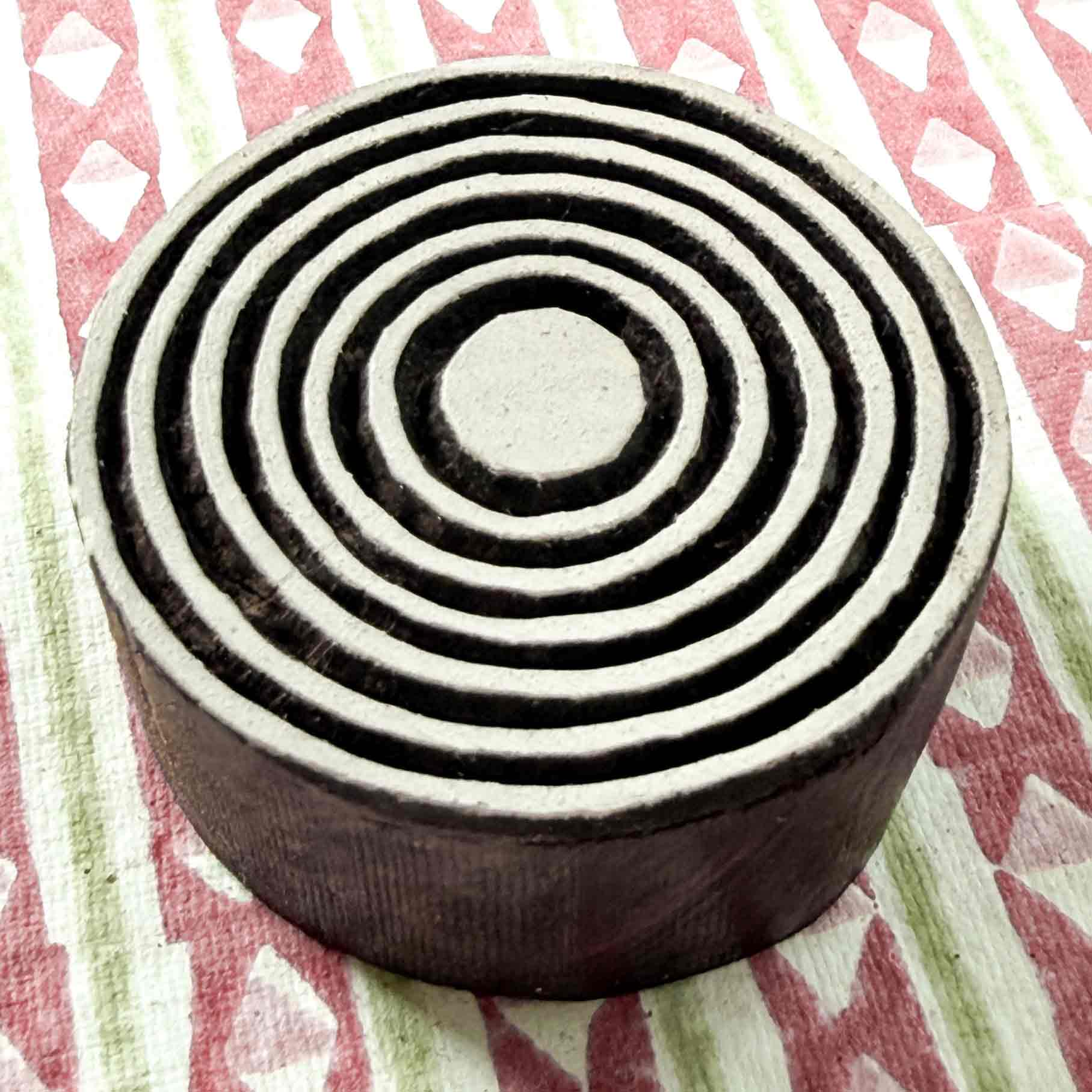 Indian wood block stamp — Bullseye Medium concentric rings resting on block printed fabric, central dot and seven evenly spaced bands, handcrafted wooden stamp, classic traditional printing block ready for printing