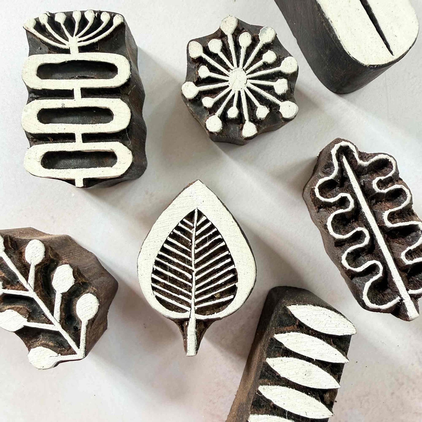 A collection of Six wooden block printing stamps with different botanical and geometric designs, arranged on a light off-white background.