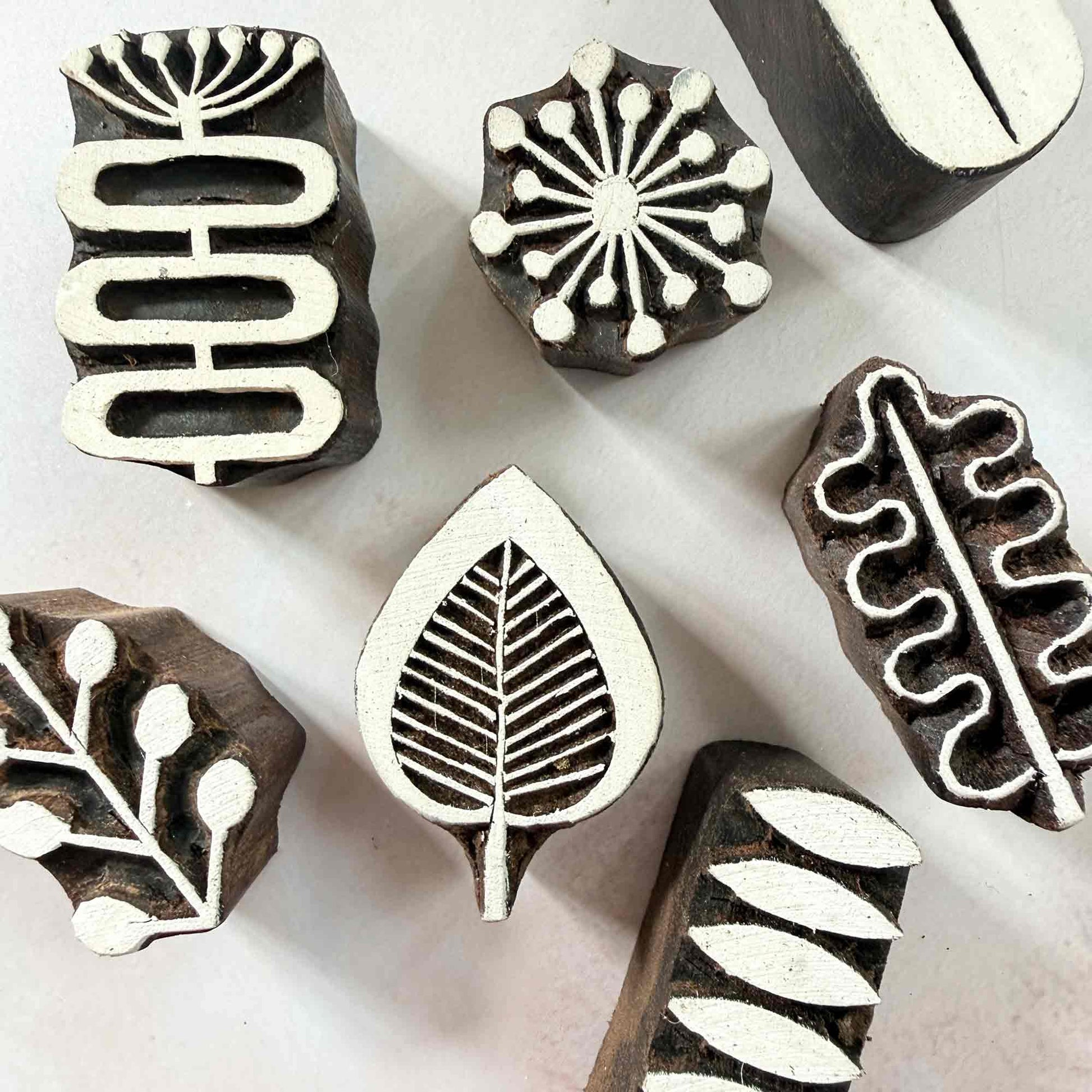 A collection of Six wooden block printing stamps with different botanical and geometric designs, arranged on a light off-white background.