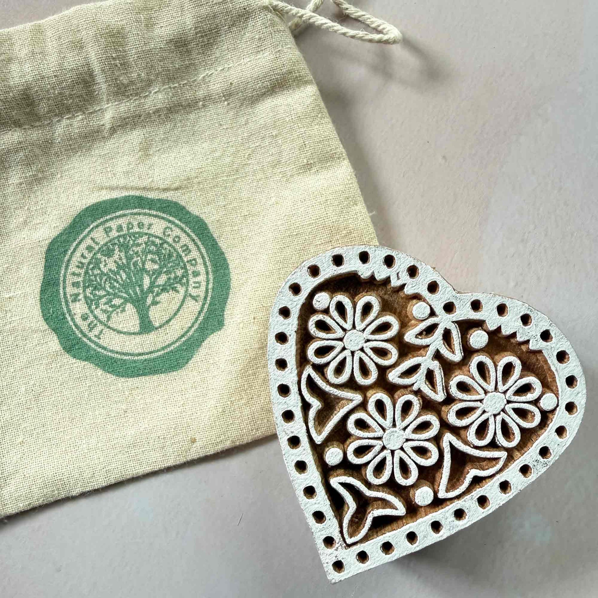 Heart-shaped wooden stamp with floral design next to a branded gift bag from The Natural Paper Company