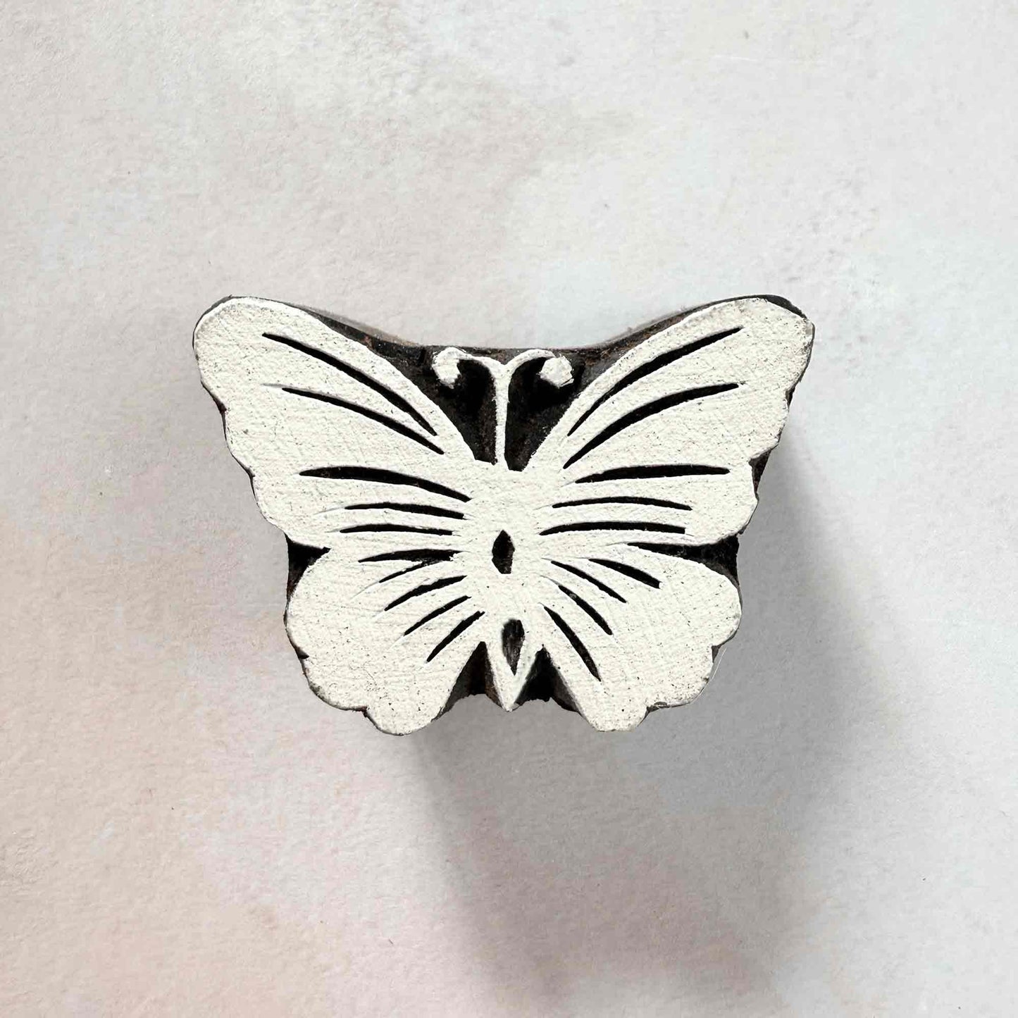 Indian wood block stamp — Flutter butterfly face-on view on soft pale background, symmetrical wings with fine curved veins, hand-carved wooden stamp, classic traditional printing block nature motif