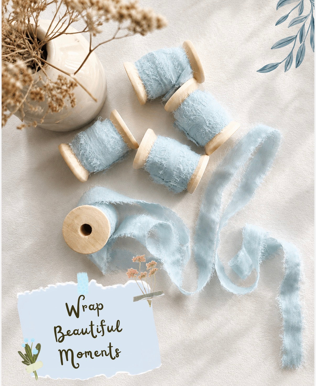 Flat-lay arrangement of soft pale blue frayed silk ribbon, 1cm wide with 5 meters per reel, presented on smooth wooden spools. One length is unfurled to display its delicate, feathered edges. Overlaid text: “Wrap Beautiful Moments”. Styled with neutral tones, dried botanicals and a ceramic vase, from The Natural Paper Company.