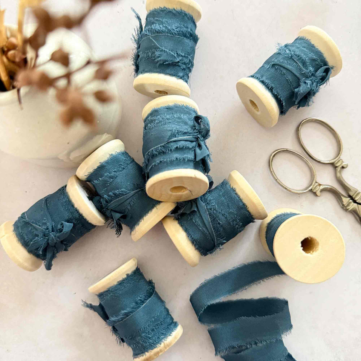 : Navy raw edge silk ribbon displayed on wooden reels with vintage scissors
