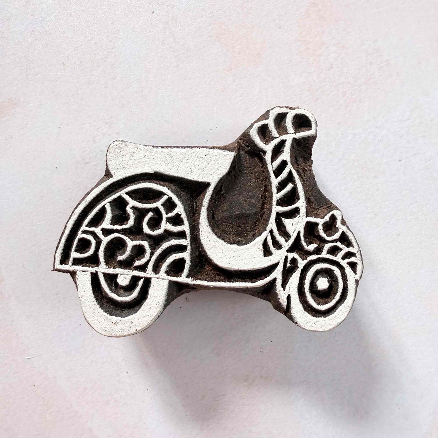 Indian wood block stamp — Scoot decorative scooter face-on view on soft pale background, scrollwork wheels and graceful curves, hand-carved wooden stamp, authentic traditional printing block from India