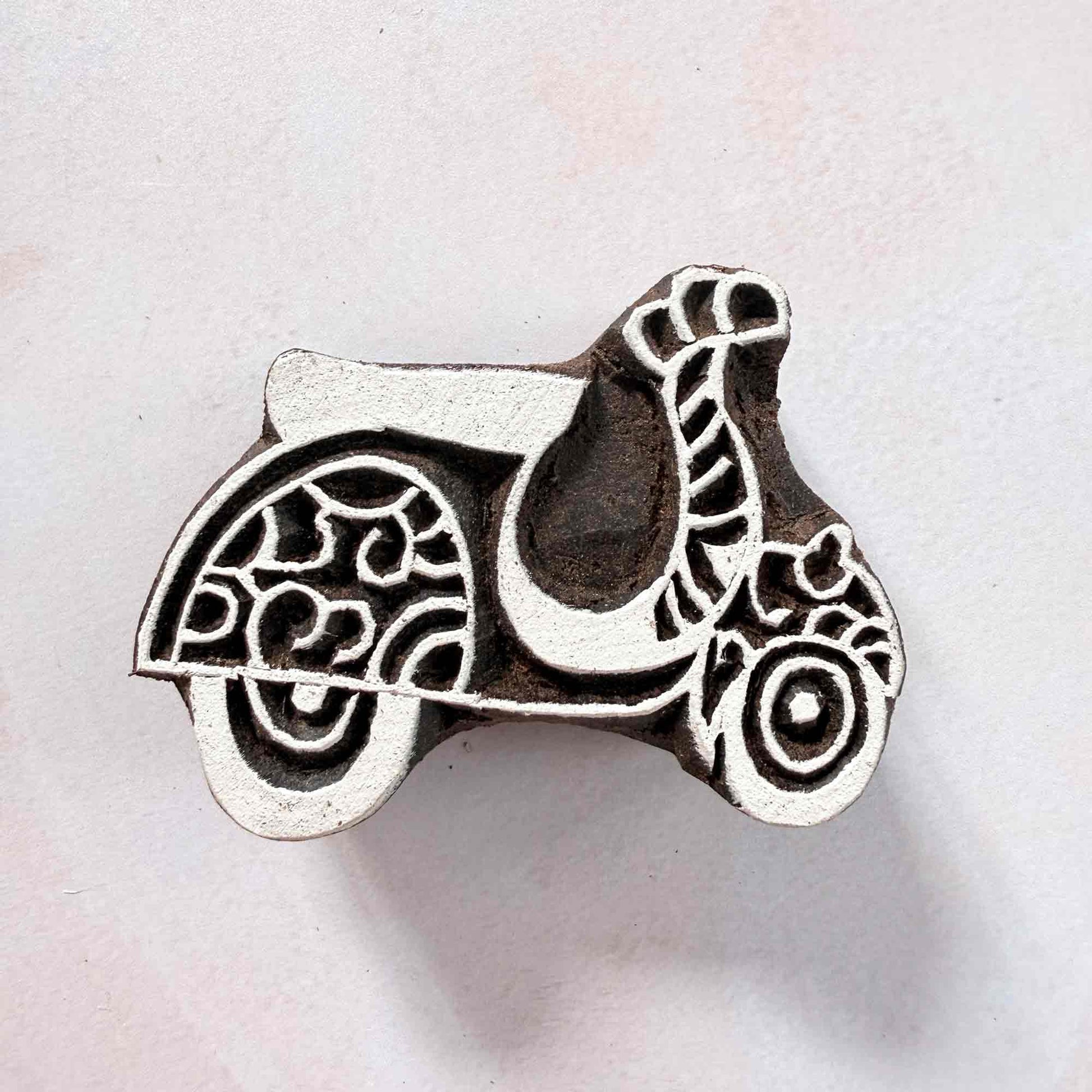 Indian wood block stamp — Scoot decorative scooter face-on view on soft pale background, scrollwork wheels and graceful curves, hand-carved wooden stamp, authentic traditional printing block from India
