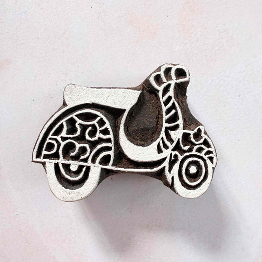 Indian wood block stamp — Scoot decorative scooter face-on view on soft pale background, scrollwork wheels and graceful curves, hand-carved wooden stamp, authentic traditional printing block from India