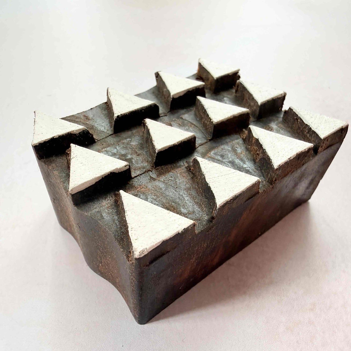 Hand-carved Tiptop Indian wood block stamp — three rows of upward triangles viewed from angle, showing carved depth and sharp triangular form, repeat-pattern hardwood printing block from India