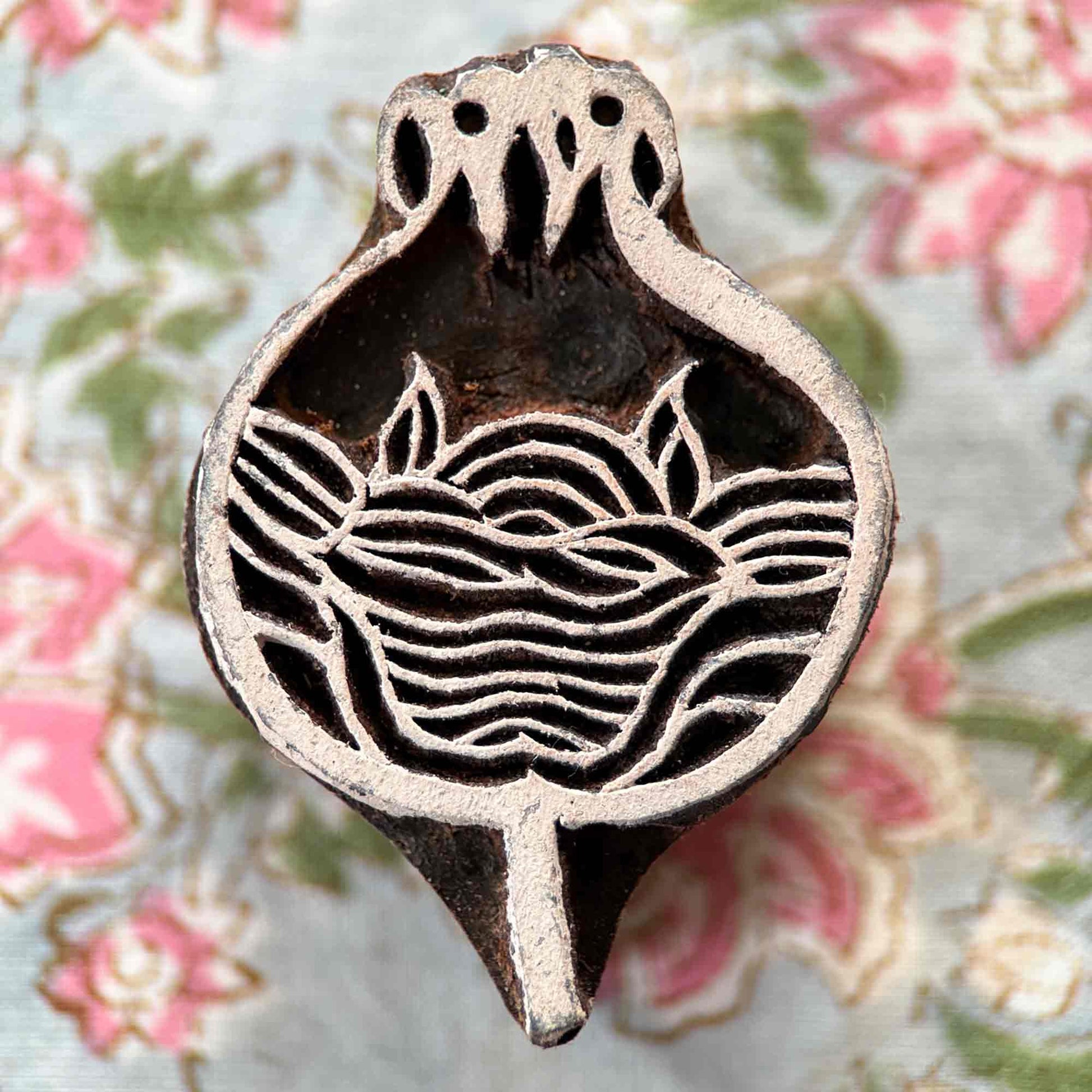 Hand-carved Anar pomegranate Wooden Stamp displayed against floral fabric, showing its detailed traditional Indian design.