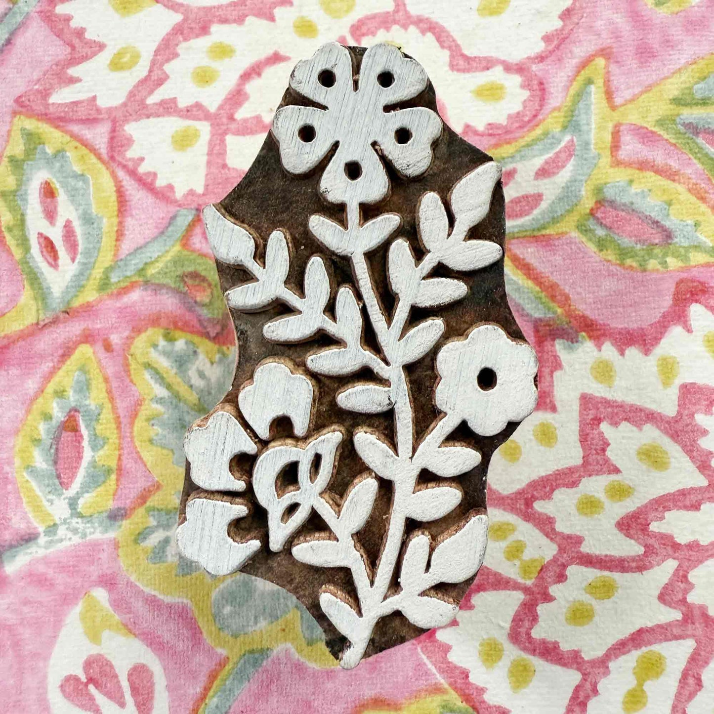 Decorative wooden stamp with floral design on a colorful fabric background