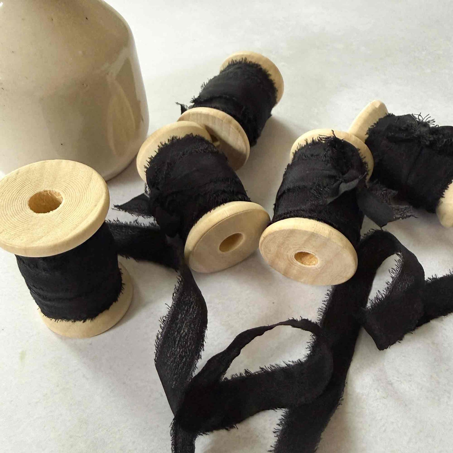 Black ribbon on wooden spools with a ceramic container on a white background