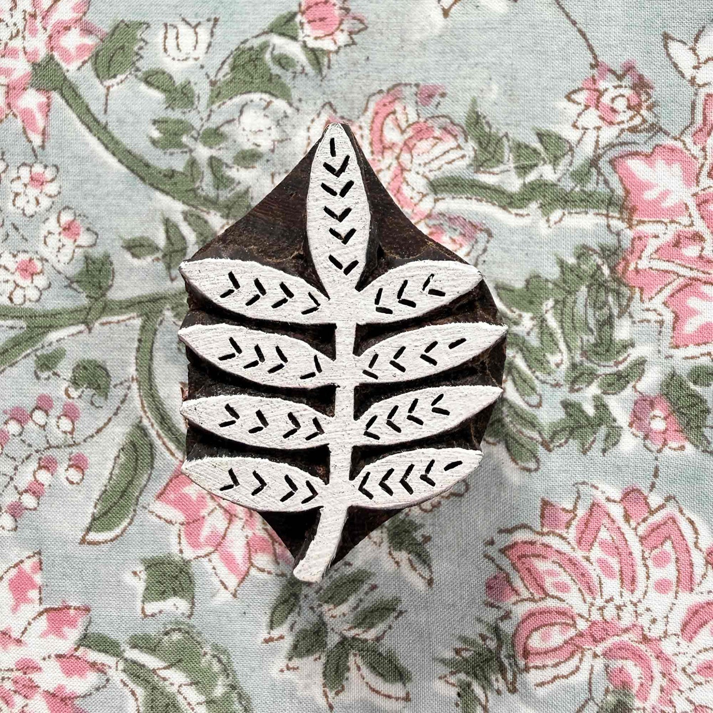 Indian wood block stamp — Bough leafy branch resting on floral block printed fabric, eight symmetrical leaflets with neat veins, hand-carved wooden stamp, classic traditional printing block botanical motif