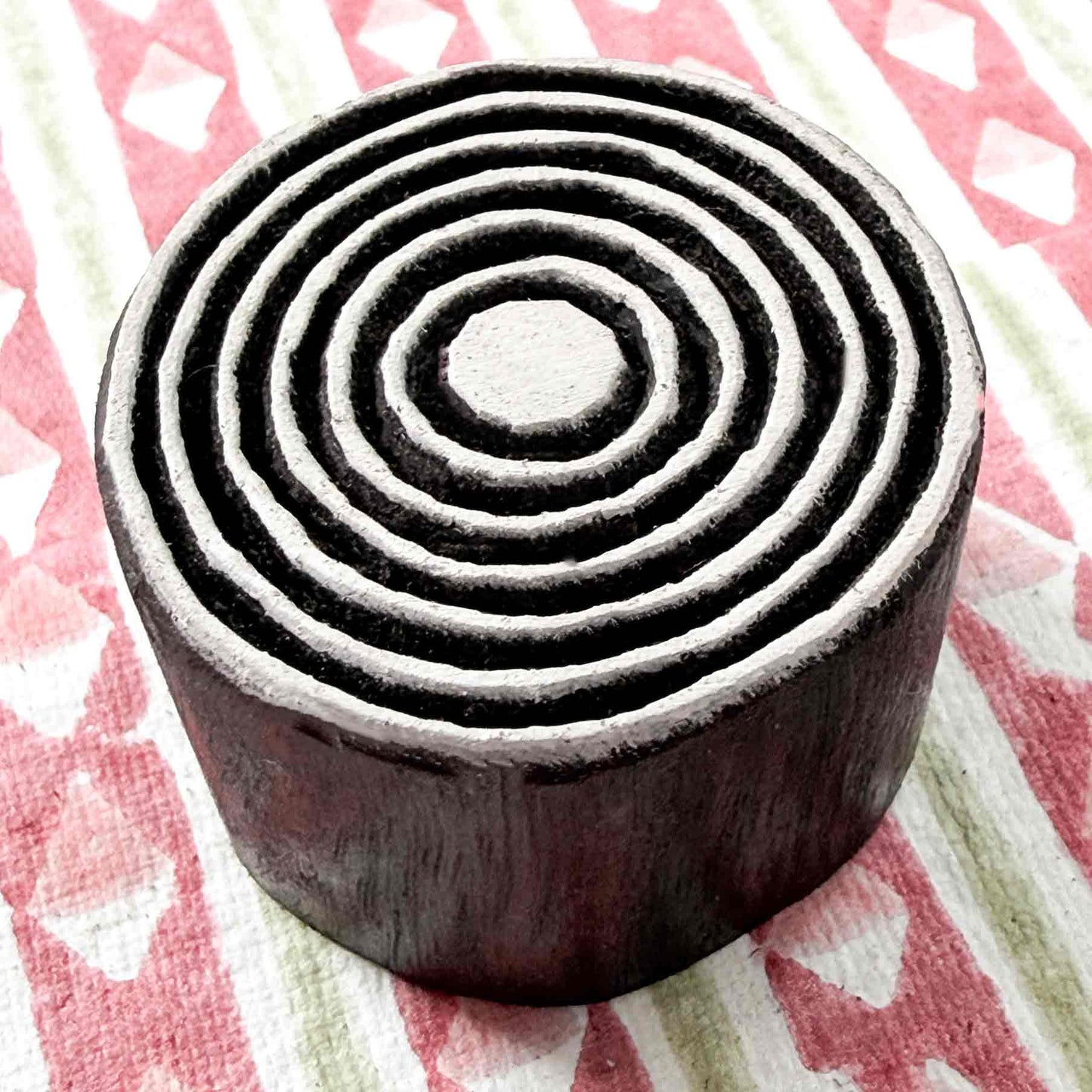 Indian wood block stamp — Bullseye Small concentric rings resting on red-and-white patterned fabric, central dot and fine evenly spaced circles, handcrafted wooden stamp, classic traditional printing block ready for printing
