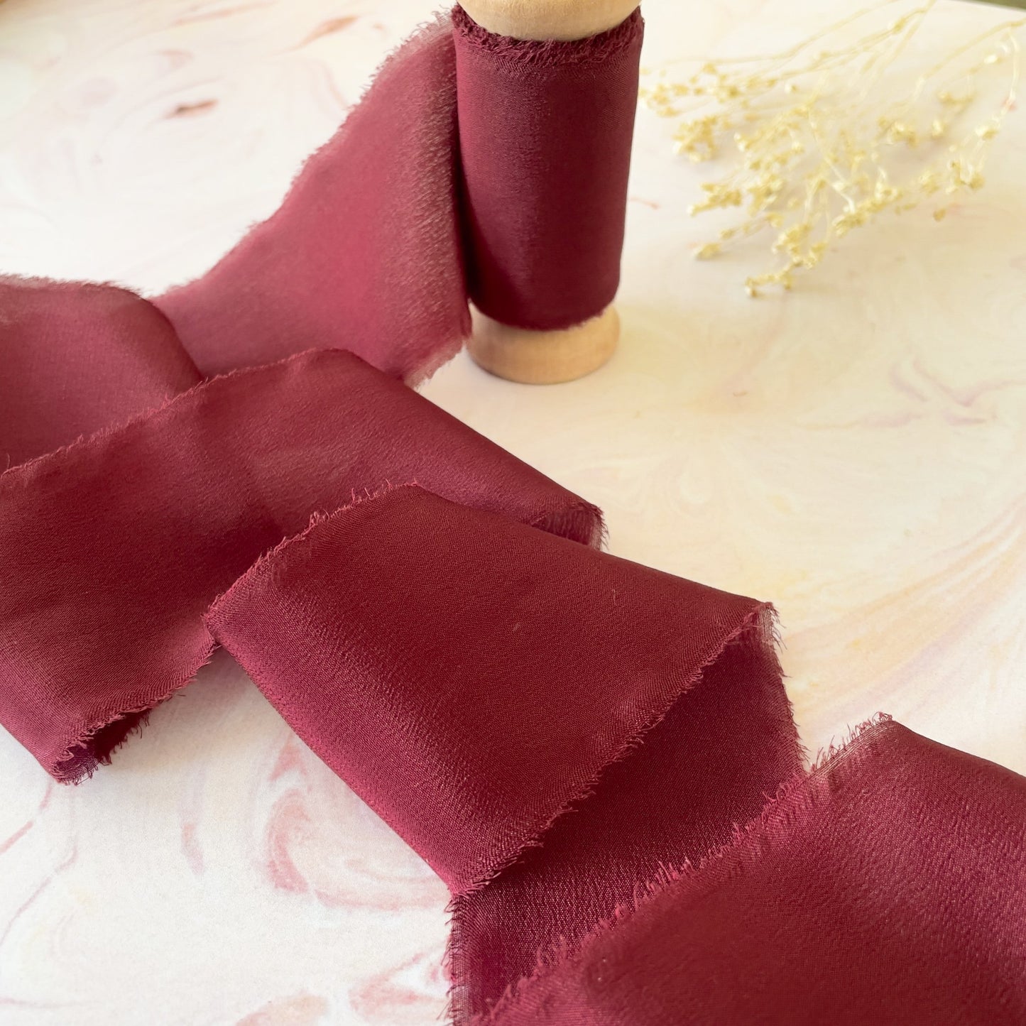 Burgundy silk ribbon for crafts.  Decorative silk ribbon with a frayed edge,  Sold on a wooden spool.  By The Natural Paper Company.