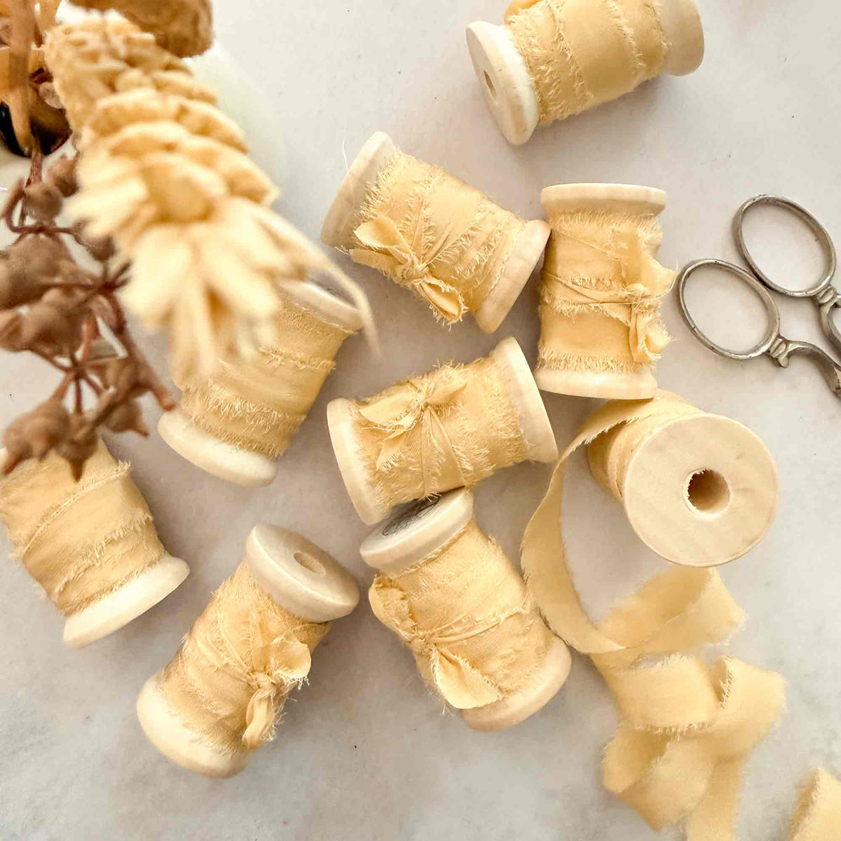 Buttermilk 10mm raw edge silk ribbon displayed on wooden reels with softly frayed edges