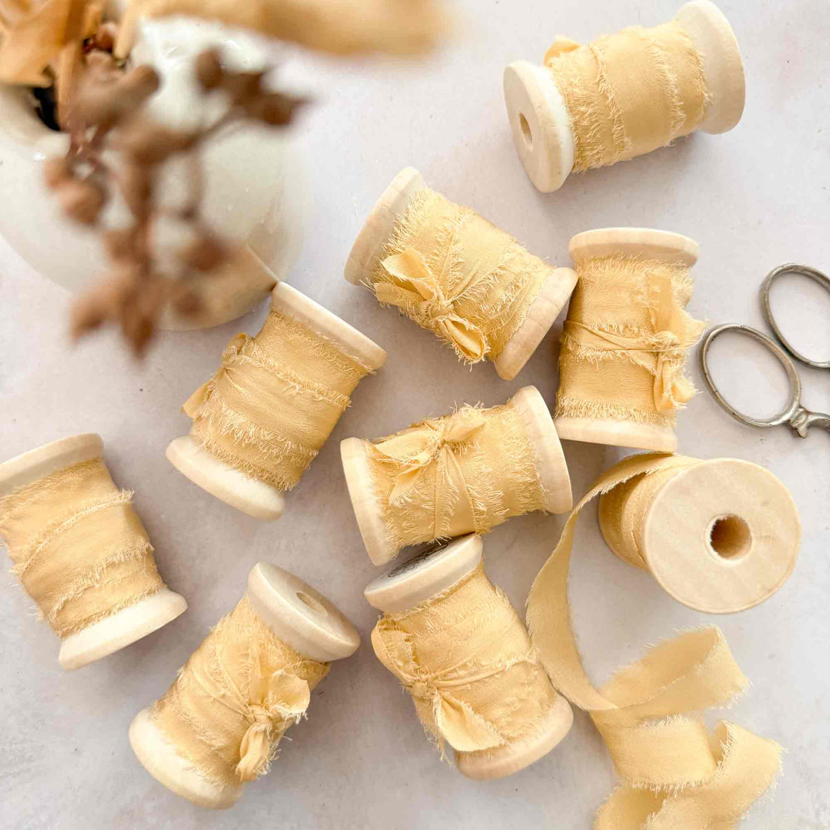 Buttermilk narrow silk ribbon displayed on wooden reels with vintage scissors