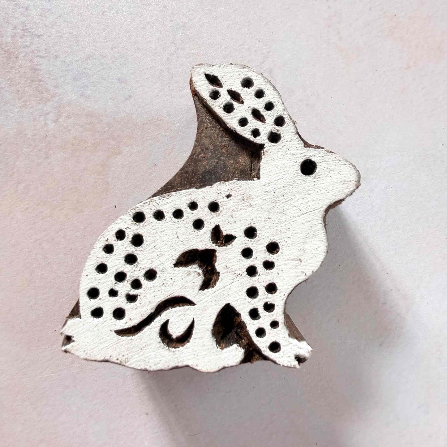 Indian wood block stamp — Cottontail spotted rabbit face-on view on soft pale background, one alert ear and fluffy tail detail, hand-carved wooden stamp, classic traditional printing block woodland motif