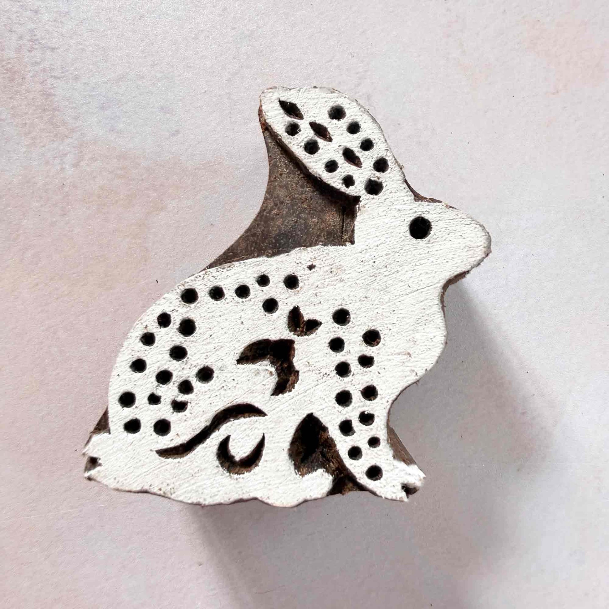 Indian wood block stamp — Cottontail spotted rabbit face-on view on soft pale background, one alert ear and fluffy tail detail, hand-carved wooden stamp, classic traditional printing block woodland motif