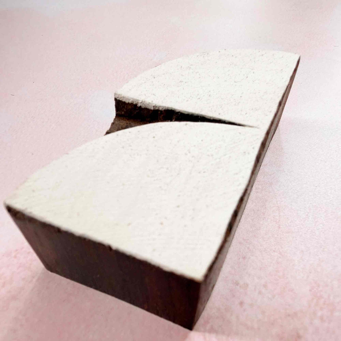 Hand-carved Crescent Indian wood block stamp — split-curve arch design viewed from side on soft pale background, traditional printing block close-up