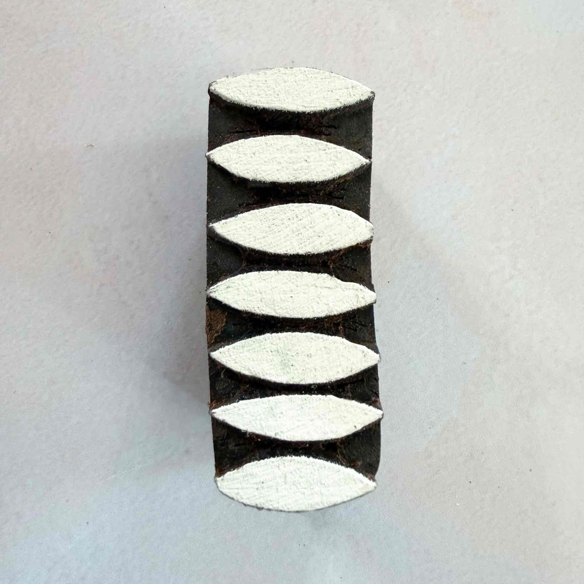 Front view of Dana Indian Wood Block Stamp measuring 5.75 x 2.25 cm with seven raised pointed oval leaf or seed-shaped motifs.
