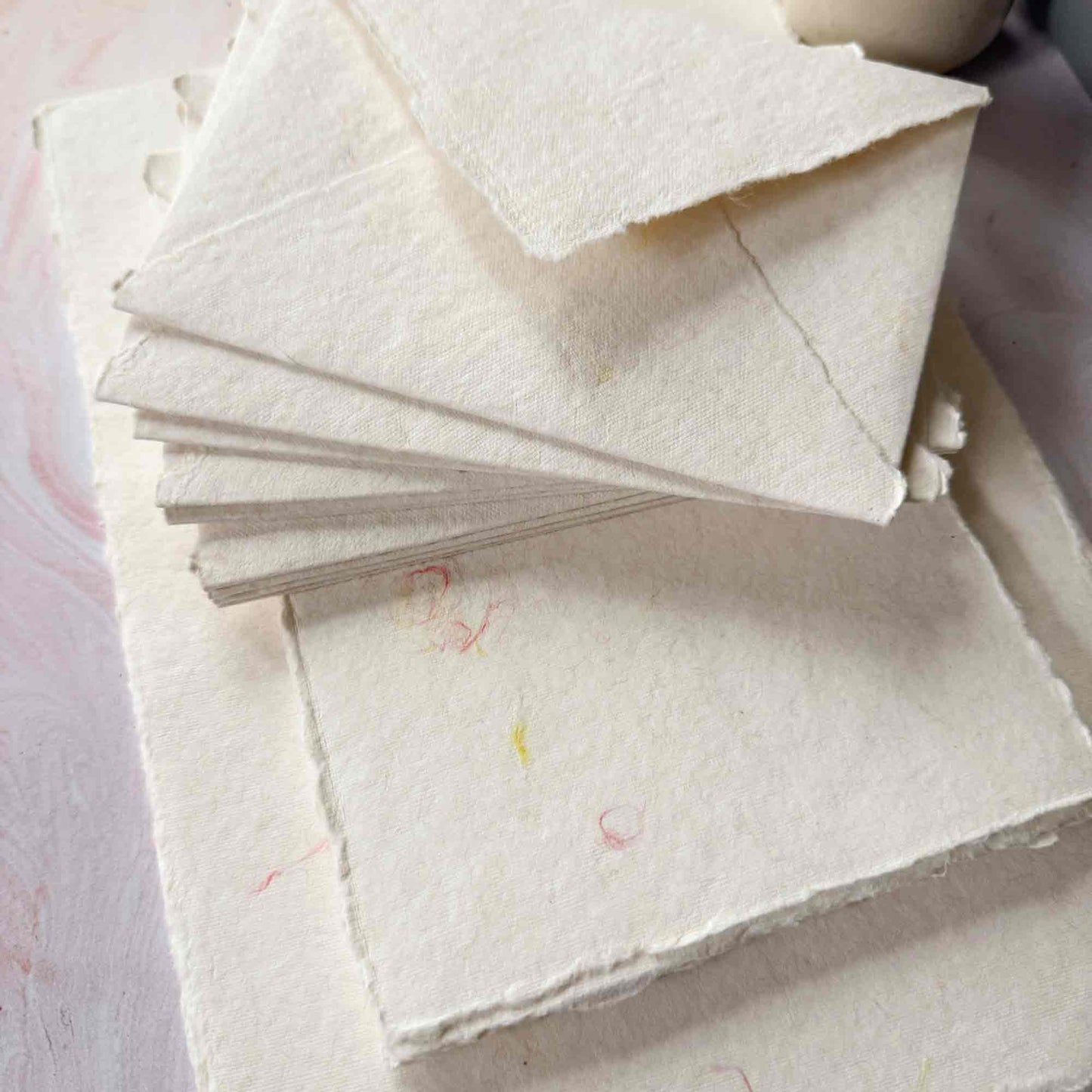 Stack of handmade cotton paper sheets with a textured surface and wool fibre decorations