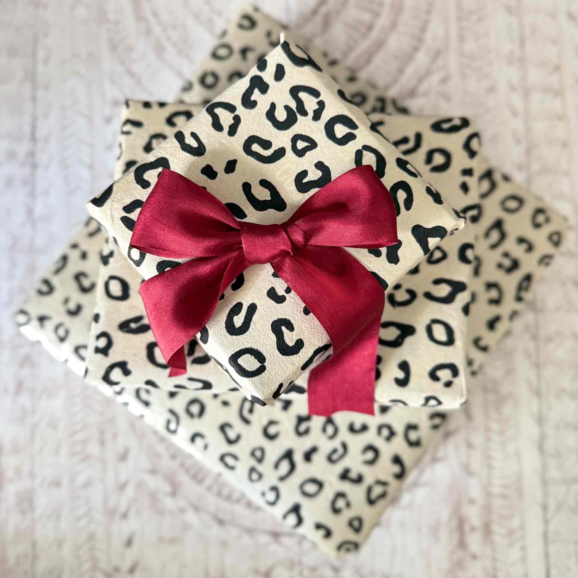 Stack of gifts wrapped in cream leopard print Lokta paper with red satin bow – handmade eco-friendly wrapping paper