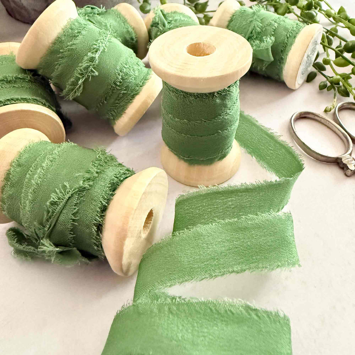 Emerald Green Habotai silk ribbon on wooden reels with frayed edges