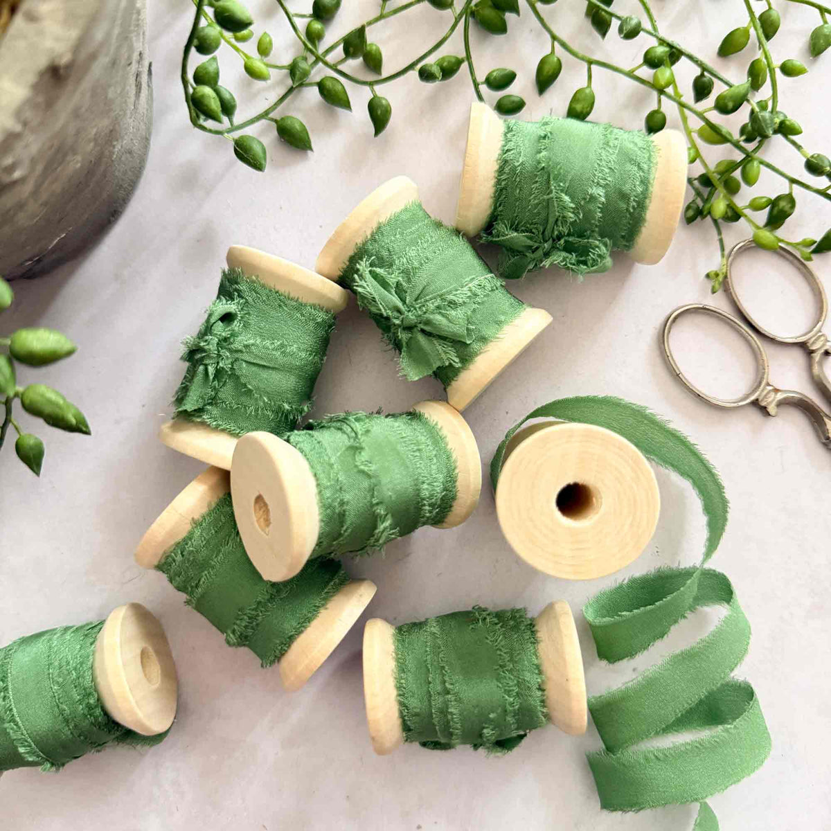 Emerald Green 10mm raw edge silk ribbon displayed on wooden reels with greenery