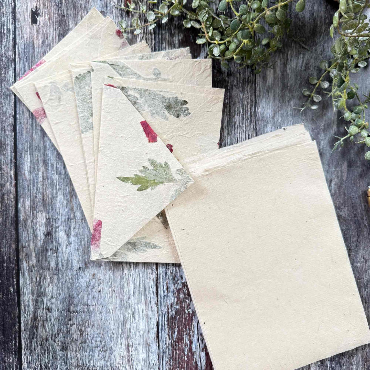 Detailed shot of Lokta paper envelopes with pressed mugwort leaves and pink bougainvillea petals, unique handmade botanical stationery