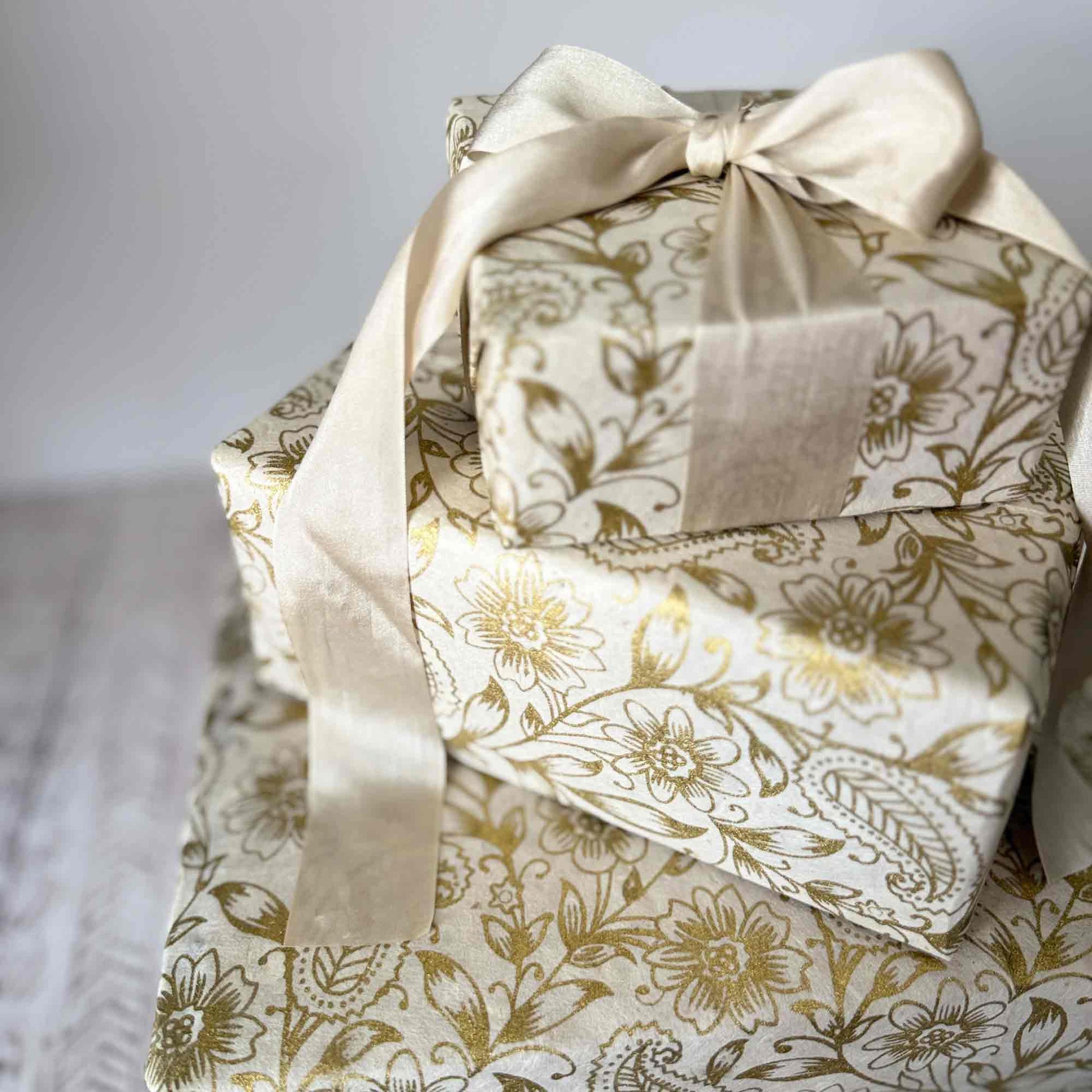 Gift boxes wrapped in handmade Lokta wrapping paper with gold floral and paisley pattern, tied with cream satin ribbon