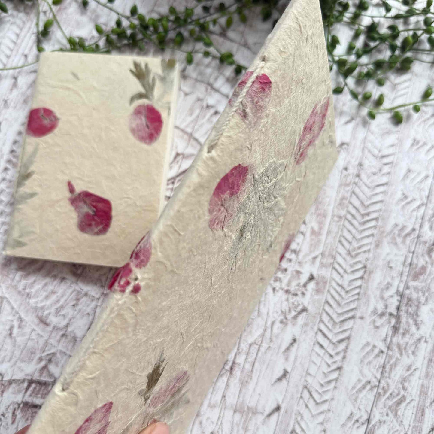 Side view of botanical Lokta notebook displaying traditional hand‑stitched spine, natural paper with pressed Mugwort leaves and Bougainvillea petals