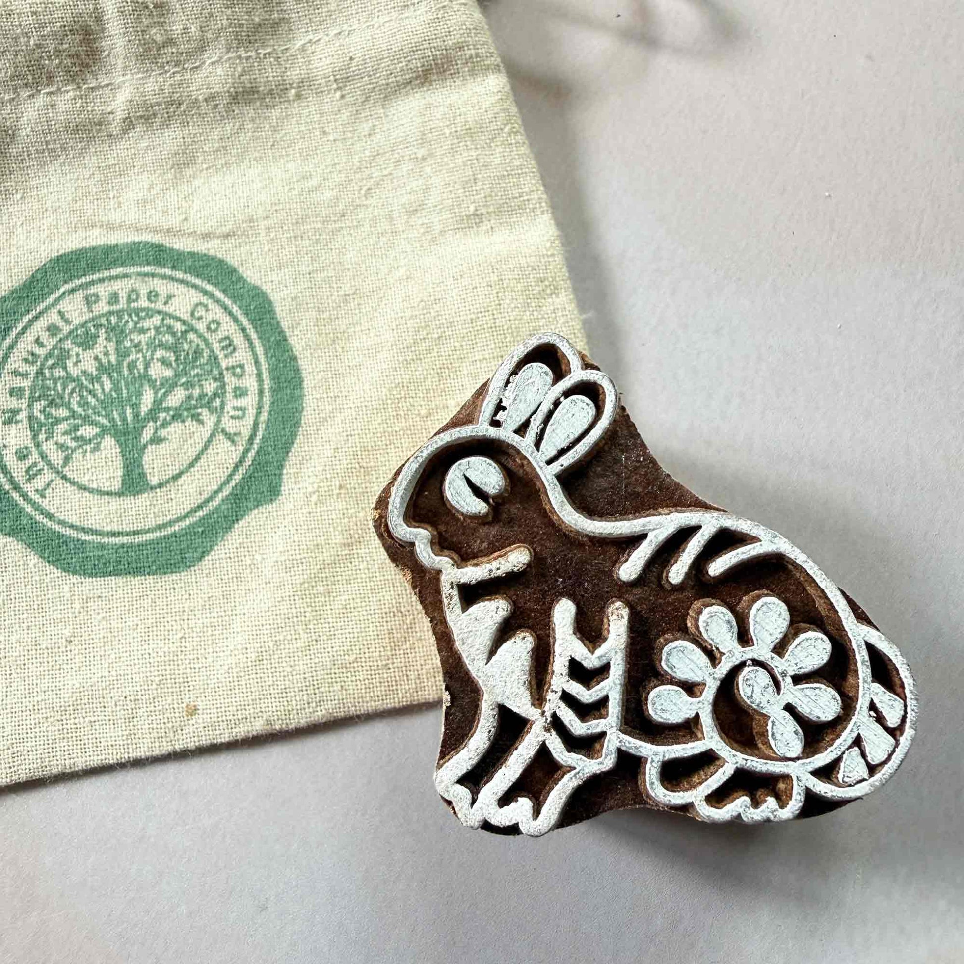 Wooden stamp with rabbit design next to a natural paper company gift bag