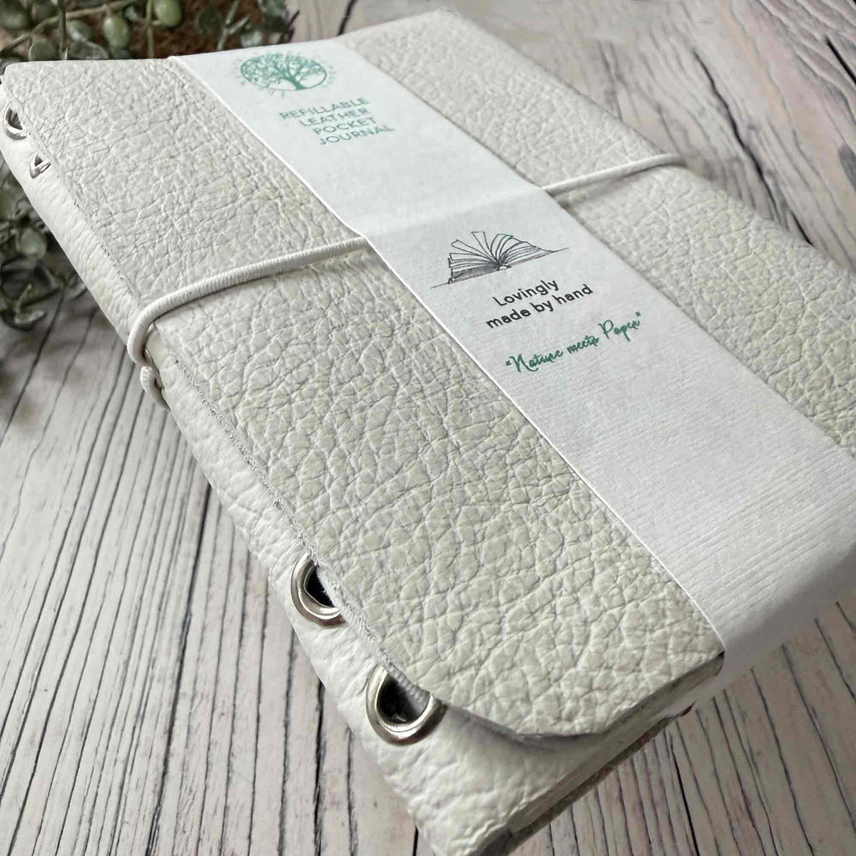 Close-up of textured ivory refillable leather journal with elastic binding and metal eyelets