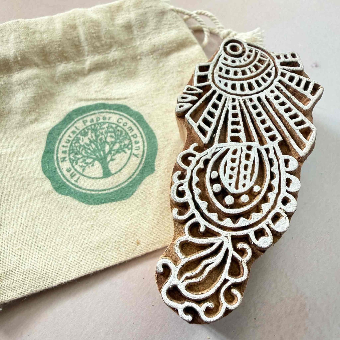 Decorative wooden stamp with intricate design next to a branded gift bag from The Natural Paper Company