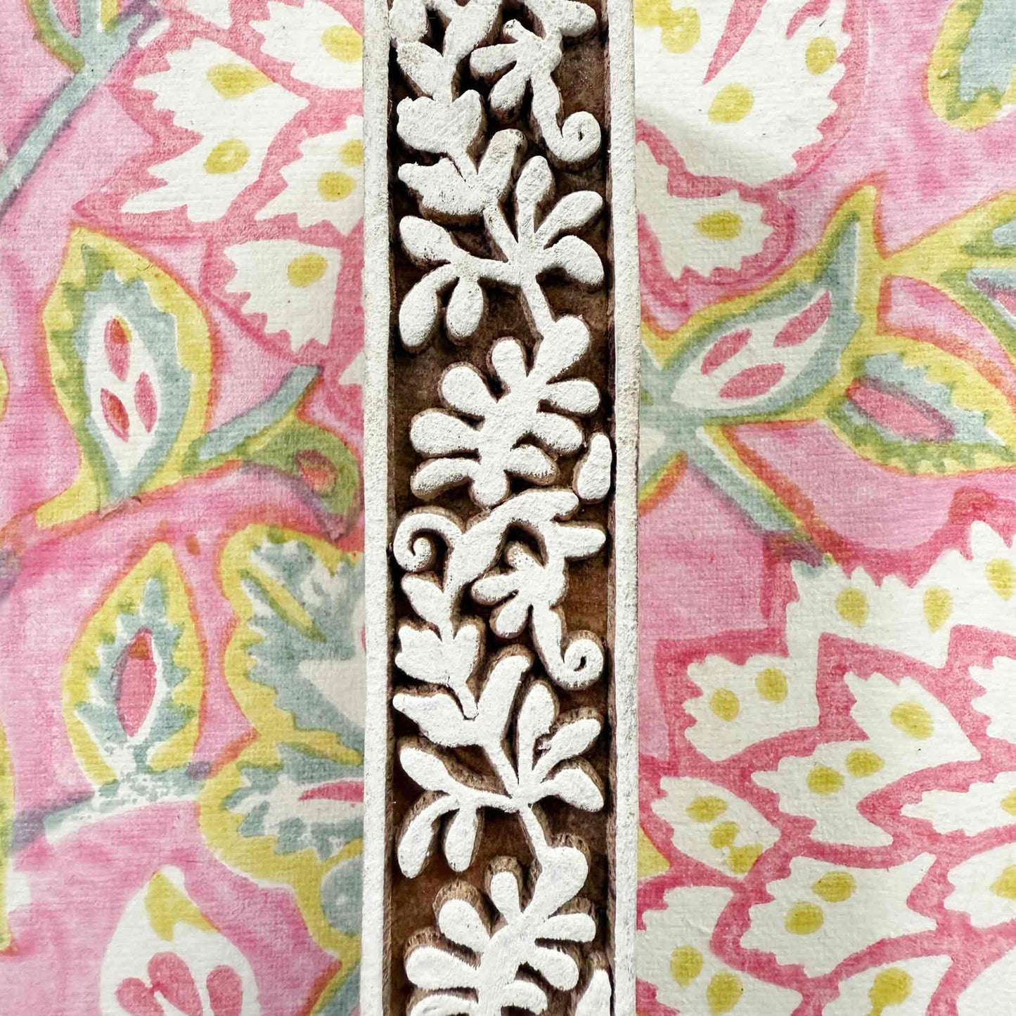 Decorative wooden printing block with floral design on a pink fabric background
