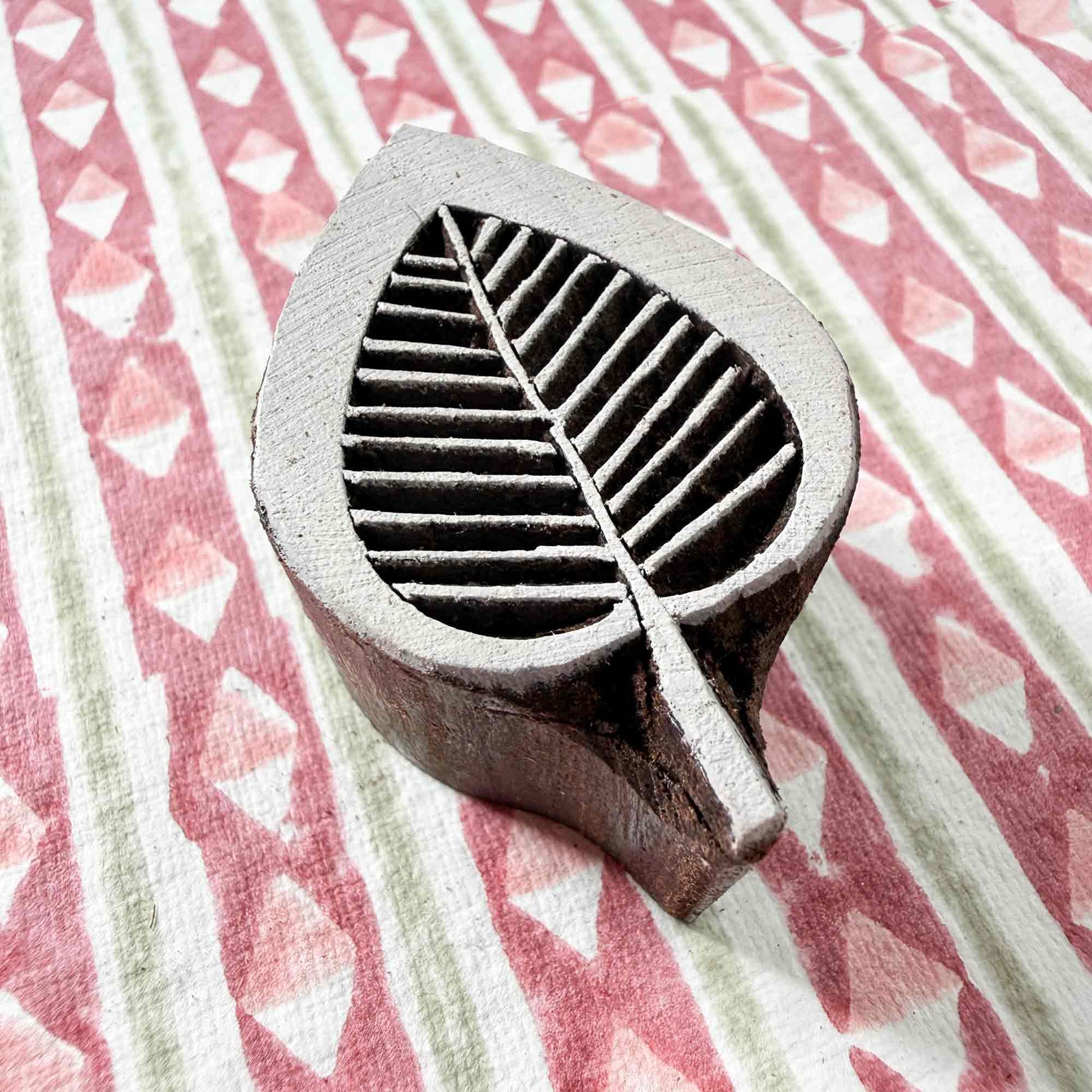Hand-carved Leaflet Indian wood block stamp — teardrop leaf with symmetrical veins resting on block printed fabric, botanical motif ready for printing, traditional hardwood printing block from India