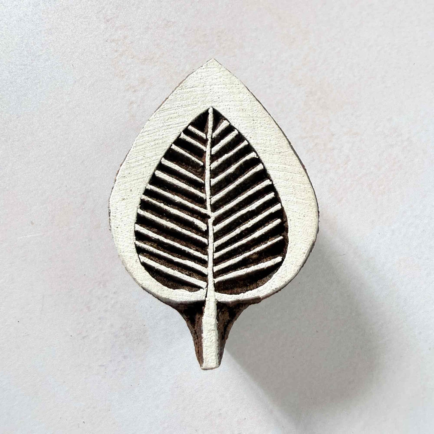 Leaflet wooden stamp — graceful veined leaf face-on view on soft pale background, fine parallel lines fanning from central vein, handcrafted Indian printing block