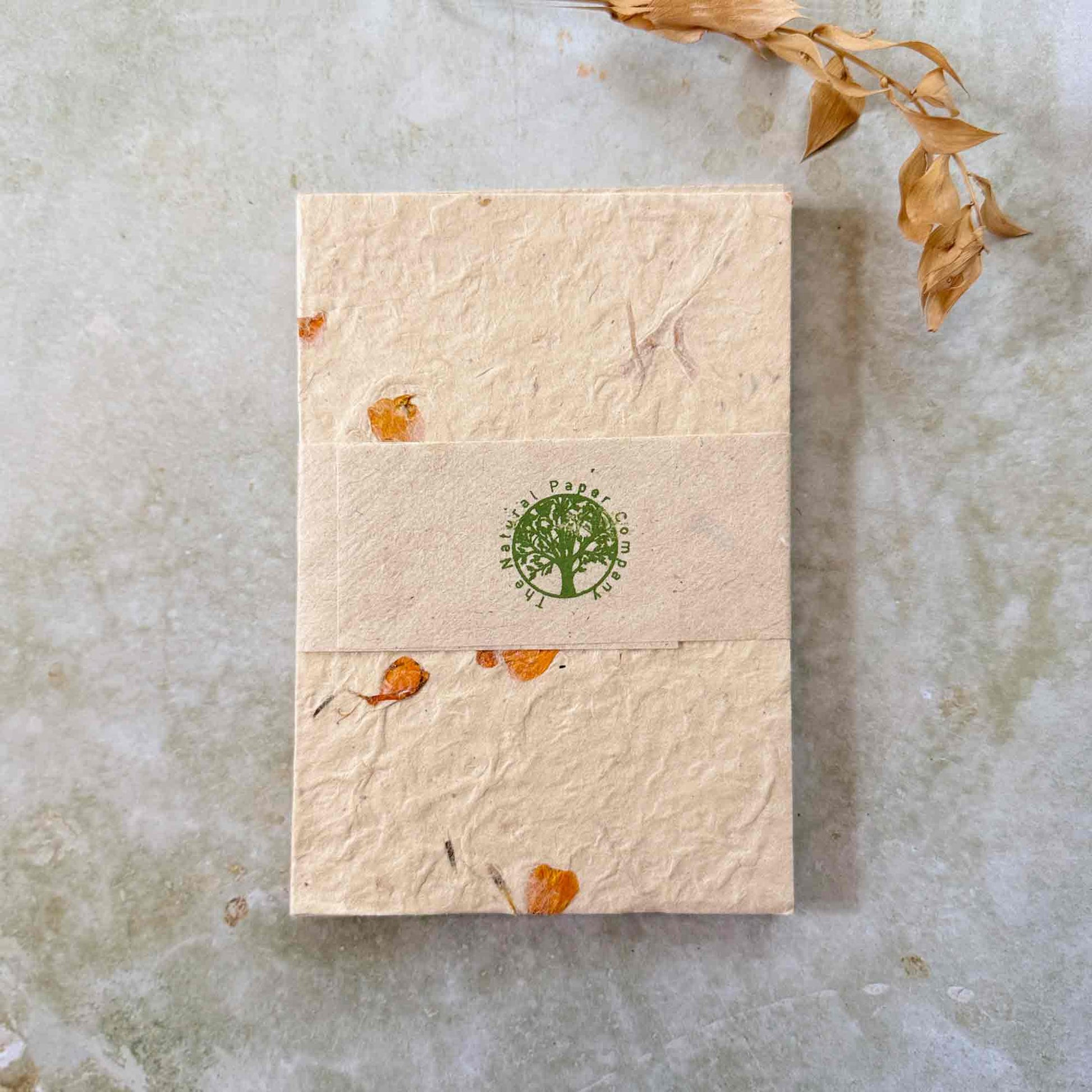 Stacked set of handmade lokta paper note cards with orange marigold inclusions, wrapped in a branded band printed with "The Natural Paper Company" logo. Tree-free, eco-friendly recycled paper.