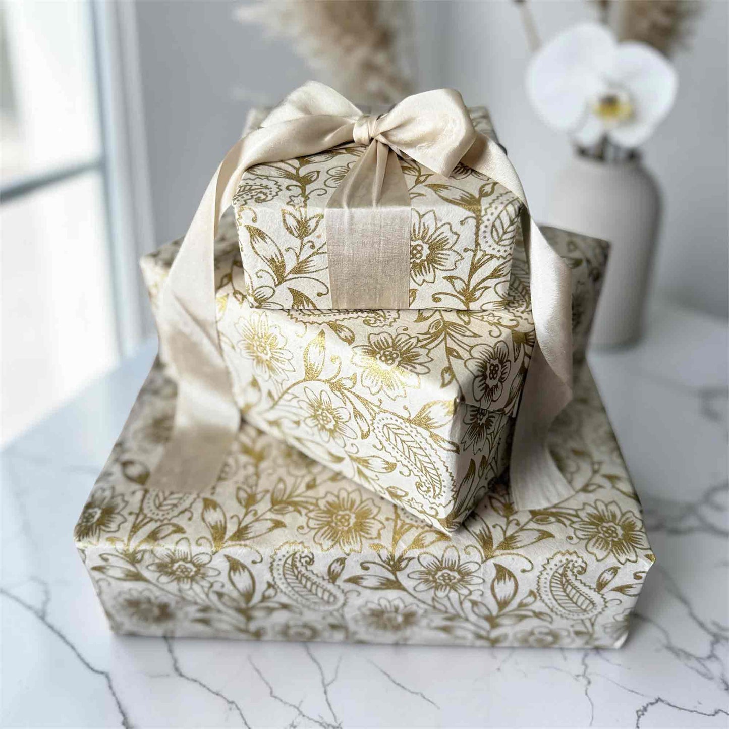 Luxury sustainable gift wrap — gold floral Lokta paper wrapping on stacked gift boxes
