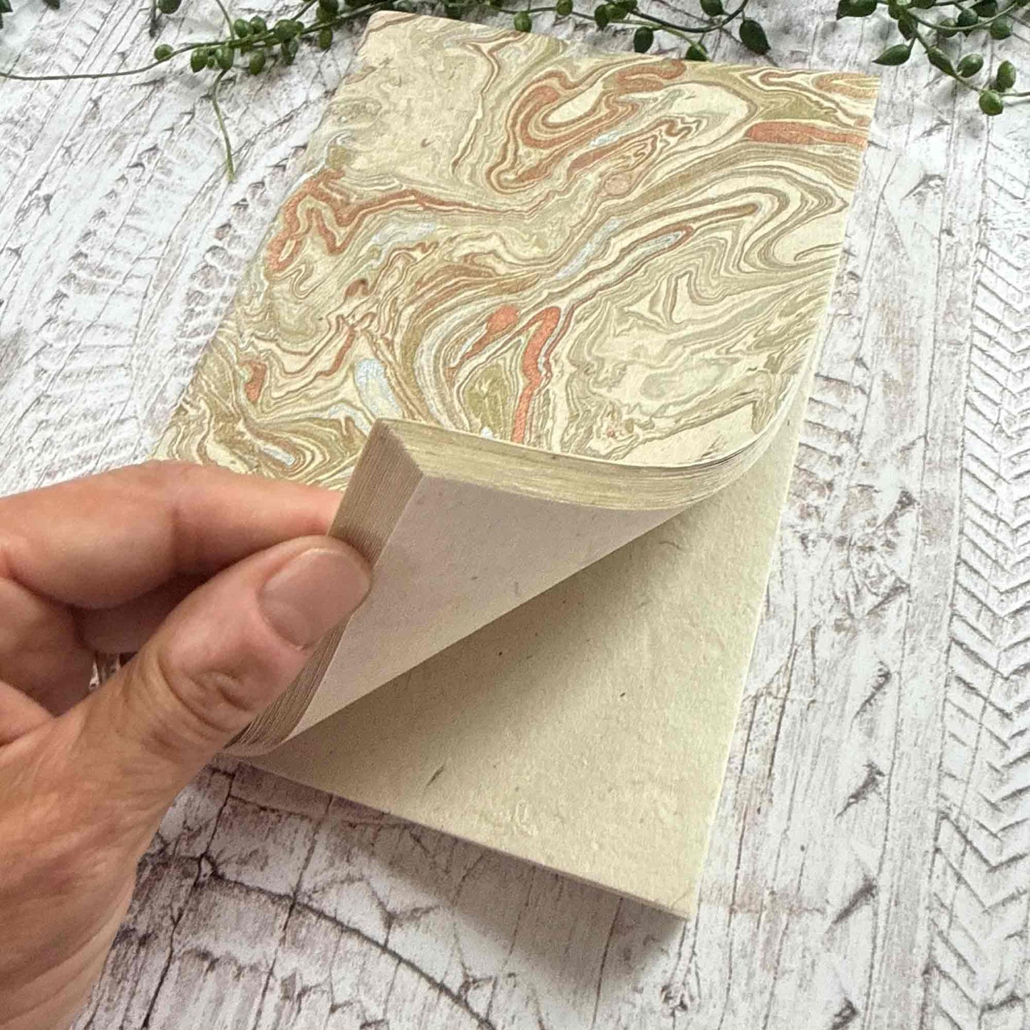 Hand opening a Midas Marble Lokta notebook, showing the soft natural texture of Lokta paper pages and the hand‑marbled gold and copper cover design