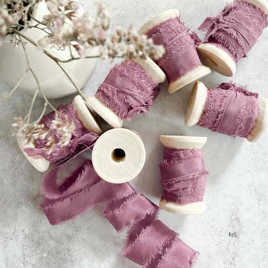 narrow silk ribbon with a raw edge.  Mauve colour silk on a wooden reel.  Fine ribbon for decorating place cards and tags