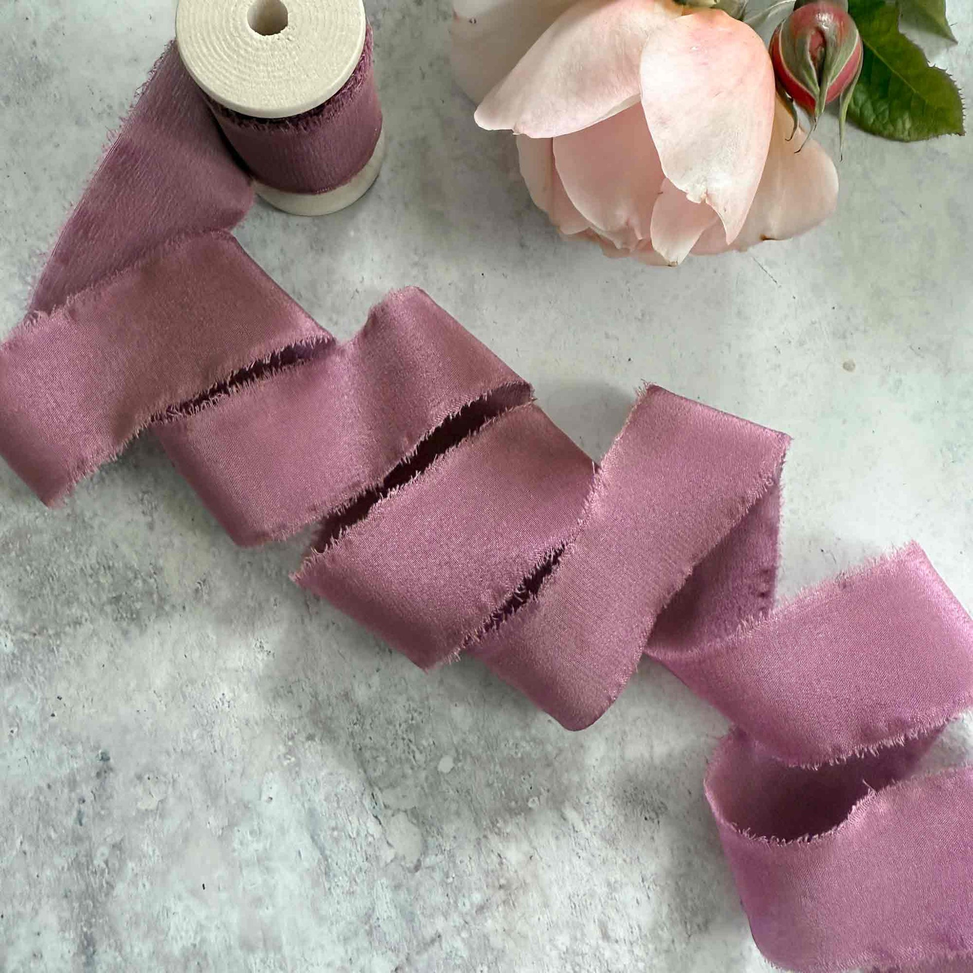 1 inch wide silk ribbon with a raw edge.  Mauve coloured ribbon on a wooden reel