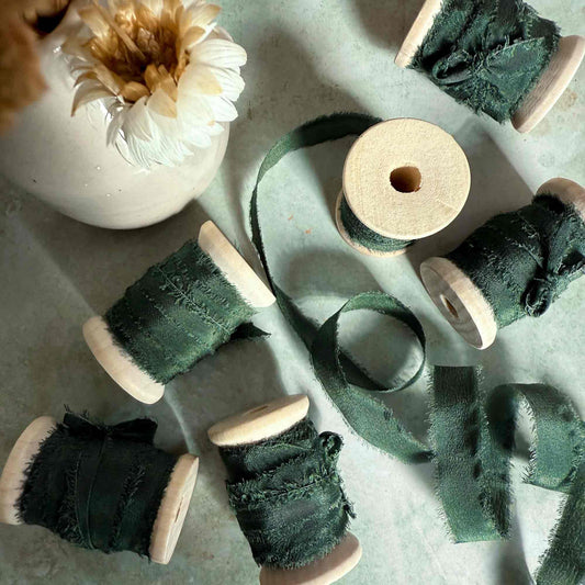 frayed edge silk ribbon on a wooden reel.  Forest green colour