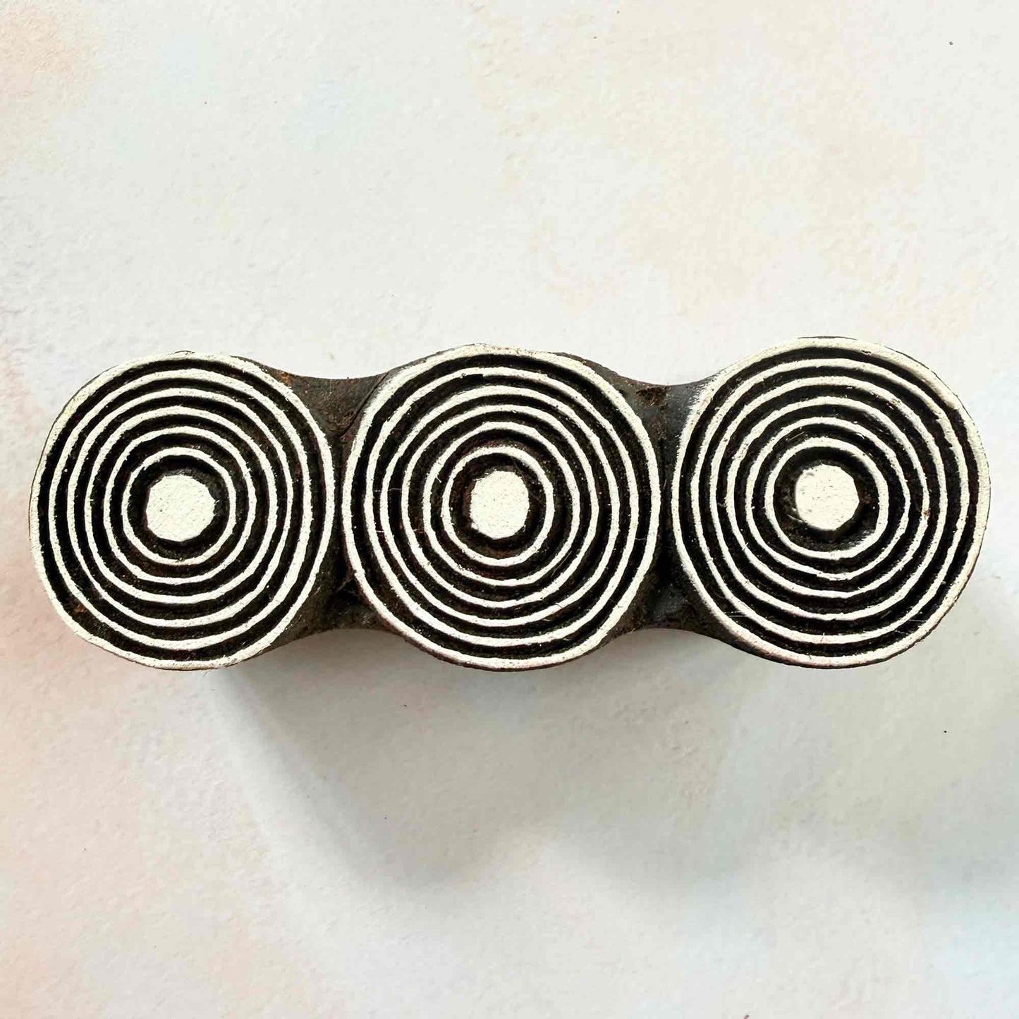 Hand-carved Orbits Indian wood block stamp — three concentric circles in a row face-on view on soft pale background, traditional printing block close-up