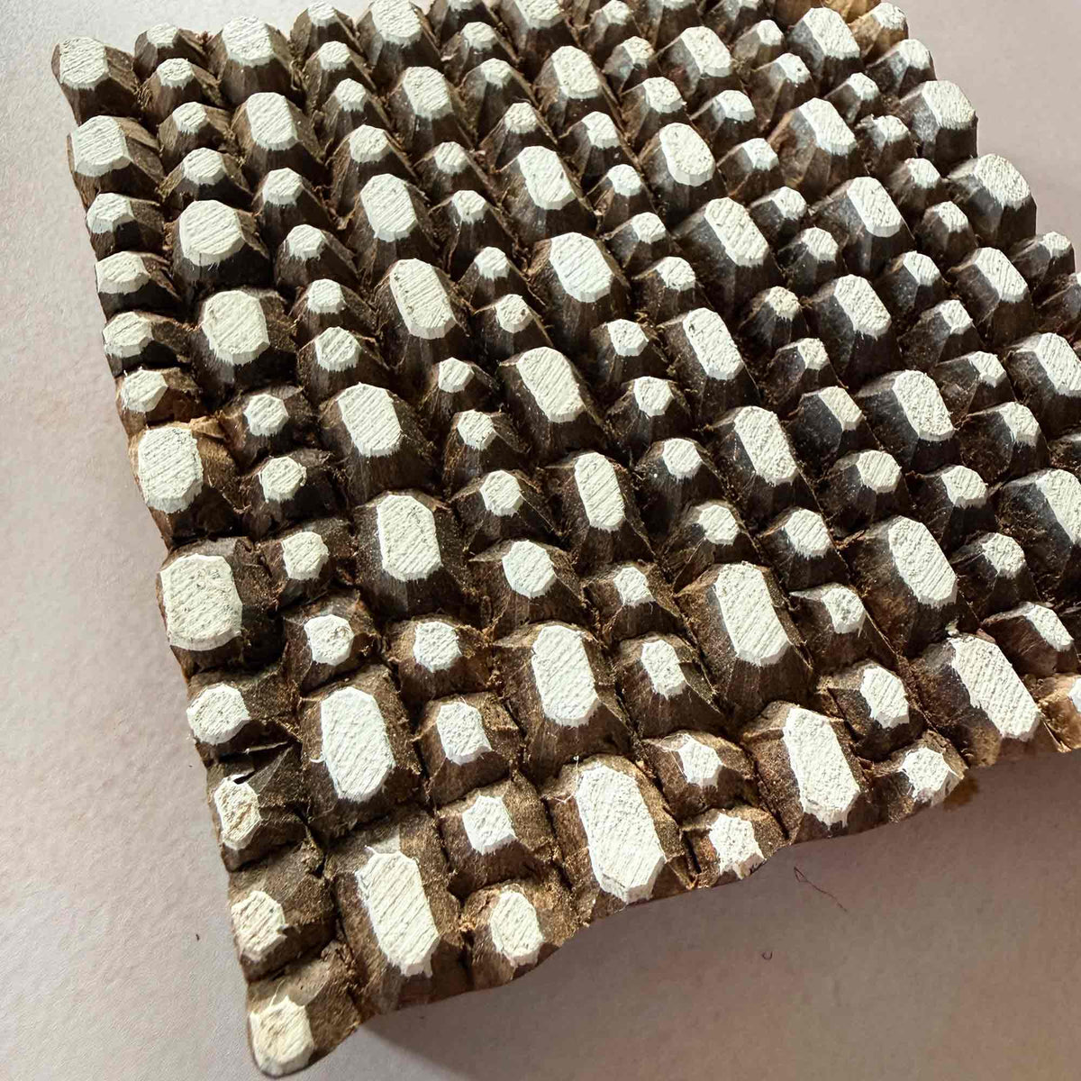 Angled close-up of Pebbles Wooden Printing Block showing raised irregular geometric shapes used to create textured fabric and paper prints.